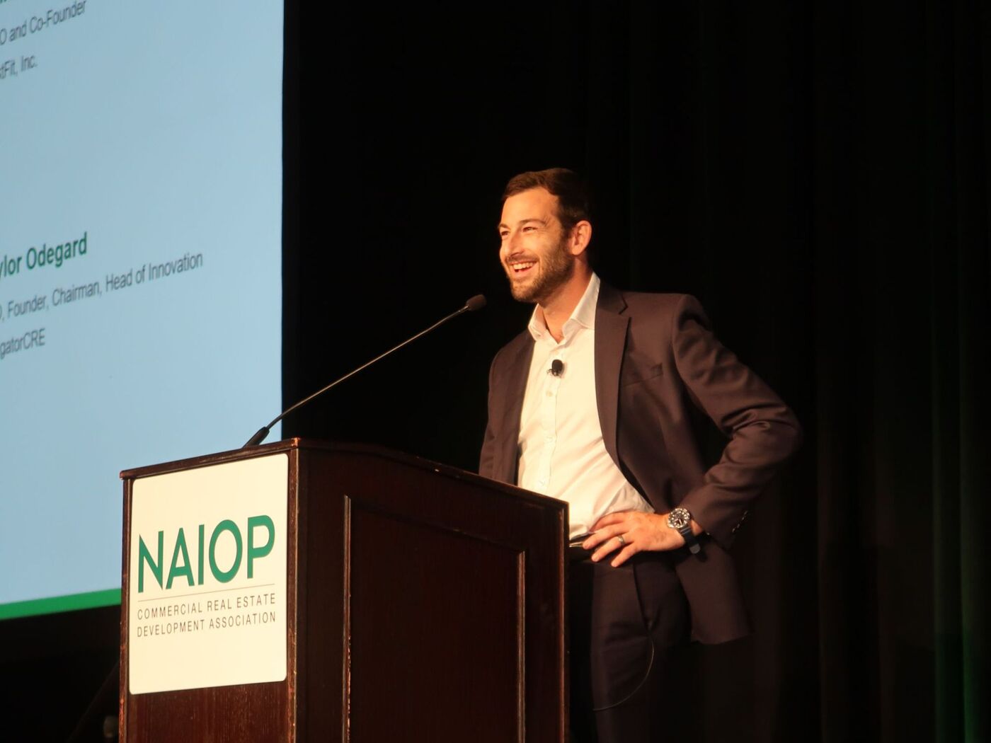 Graham at a NAIOP podium, laughing, with the panel's introduction slide on the screen behind him